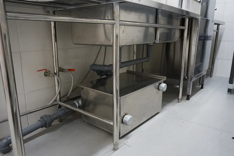 Stainless steel under-counter grease trap installed below a commercial sink